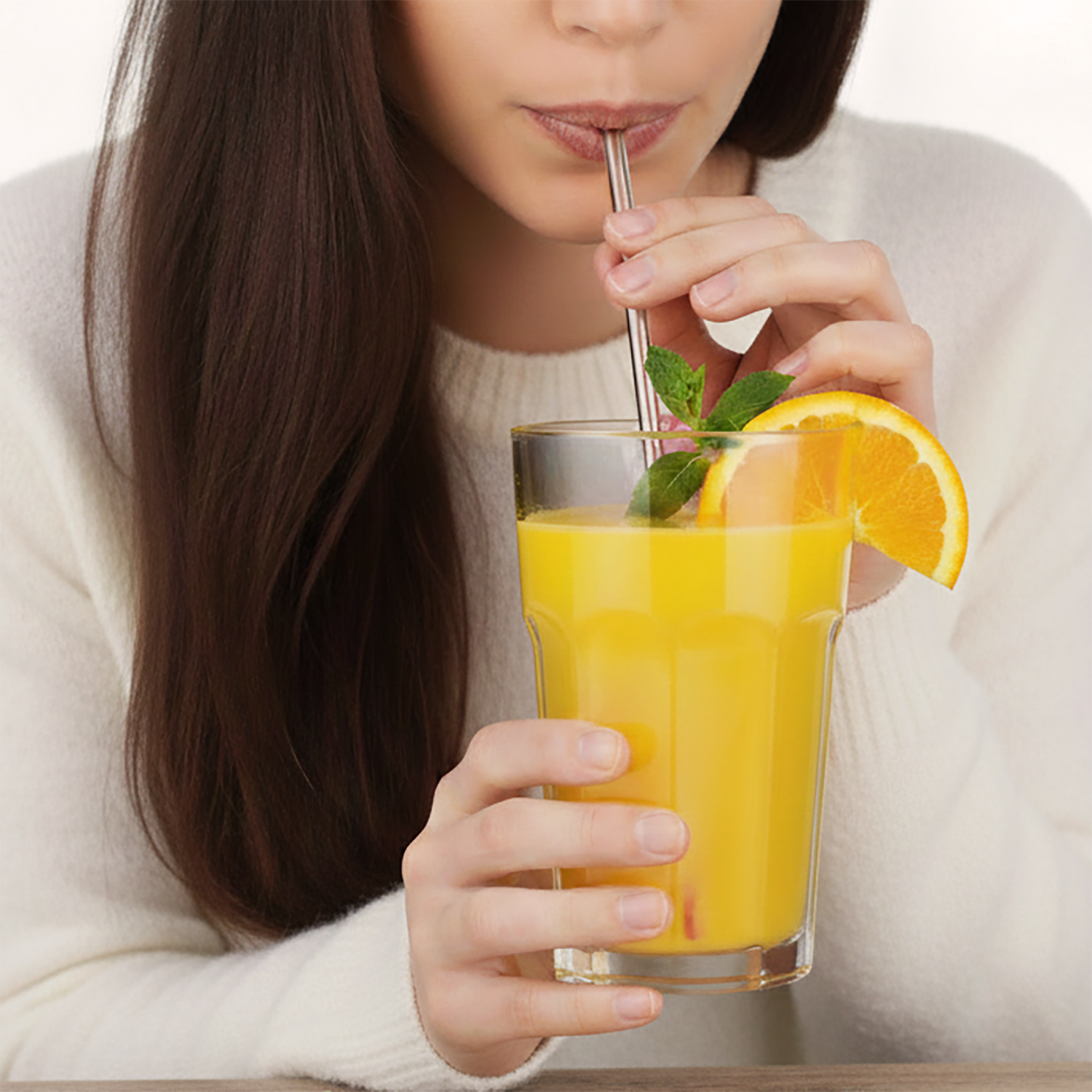 Person trinkt gelben VitalComplex-Drink aus einem Glas mit Strohhalm, Orangenscheibe und Minze